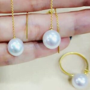 hand-holding-white-south-sea-pearls-in-18ky long-chain-earrings-and-a-pearl-ring-resting-on-table